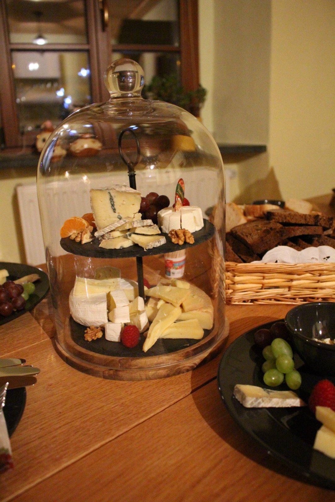Zweistöckige Käse-Etagere unter einer Glasglocke mit Trauben und Brot